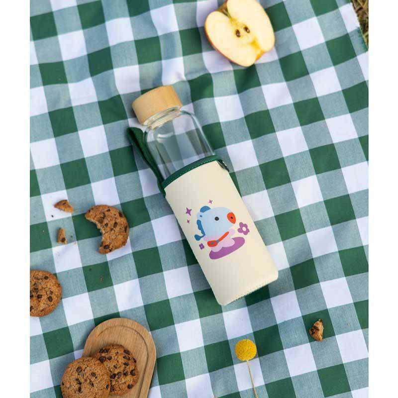 Kremowa butelka na wodę BT21 Mang w pokrowcu z postacią Mang, na kraciastym obrusie obok ciastek
