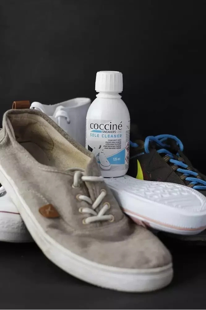Płyn czyszczący do podeszew Coccine - butelka Sole Cleaner obok zabrudzonych tenisówek i sneakersów