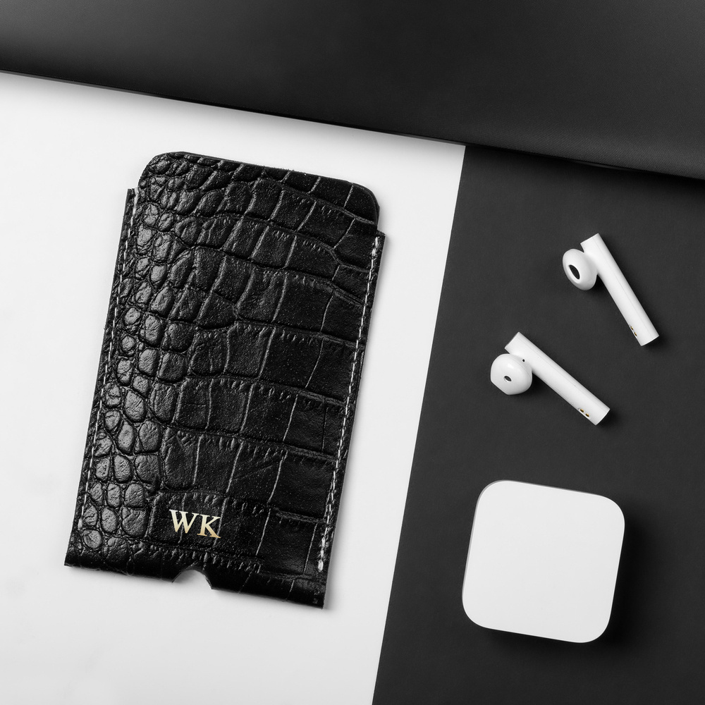 Czarne etui na iPhone 11 Solier SA58 wężowe ze złotymi inicjałami, obok słuchawek bezprzewodowych